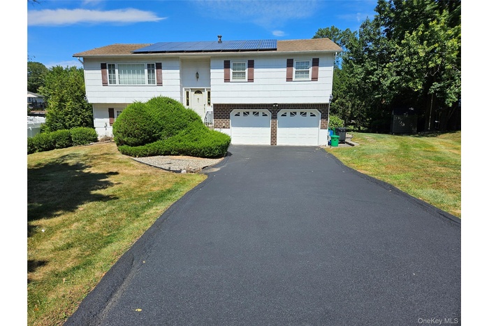 Bi-level home featuring roof mounted solar panels, driveway, an attached garage, a front lawn, and brick siding
