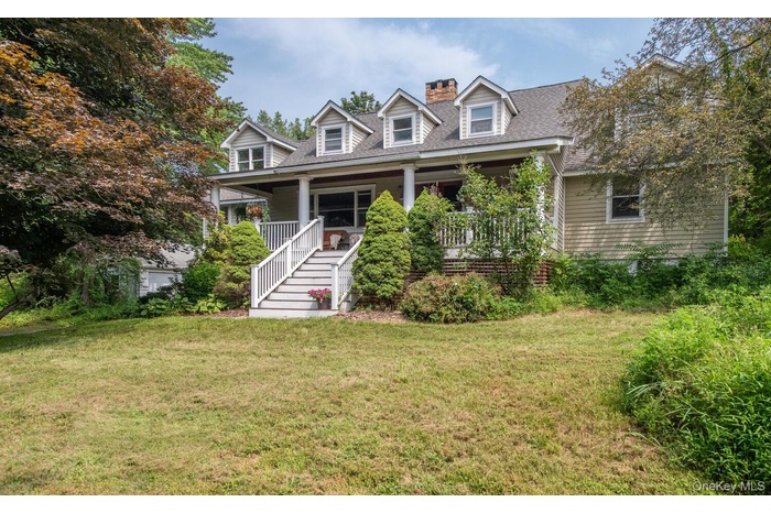 Cape cod house featuring covered porch, a front yard, a shingled roof, a chimney, and stairway