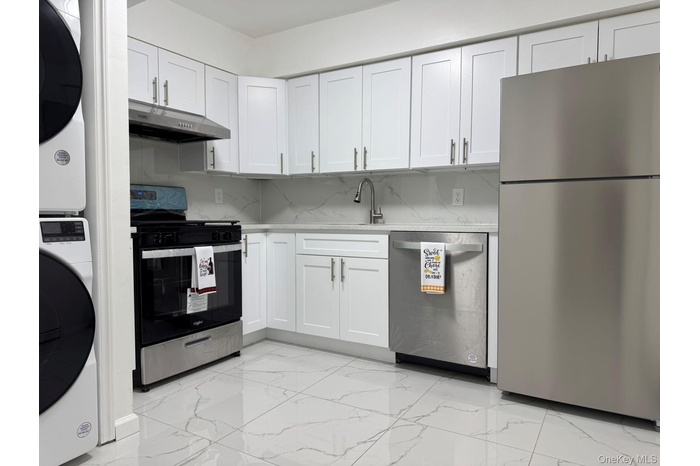 Kitchen featuring stainless steel appliances, white cabinetry, light marble finish flooring, light stone counters, and tasteful backsplash