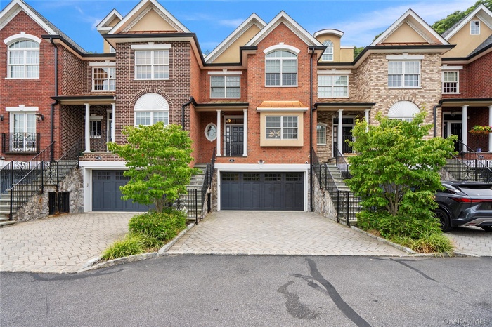 Traditional-style home with an attached garage, decorative driveway, brick siding, and stairway