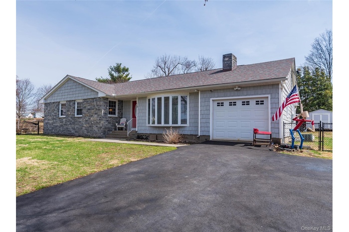 Ranch-style home featuring driveway, a chimney, an attached garage, a front lawn, and a shingled roof