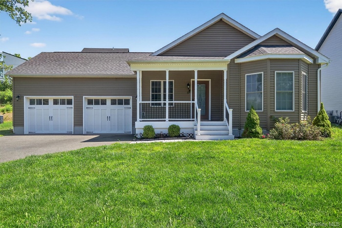 View of front facade featuring covered porch, driveway, an attached garage, a shingled roof, and a front lawn