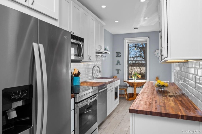 Kitchen with a sink, wood counters, appliances with stainless steel finishes, and white cabinetry