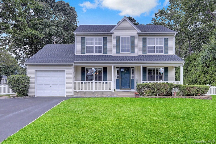 Traditional-style home featuring a porch, a garage, a front lawn, asphalt driveway, and roof with shingles
