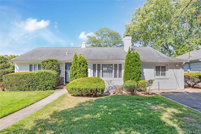 Ranch-style home with a chimney, a front lawn, a shingled roof, and brick siding
