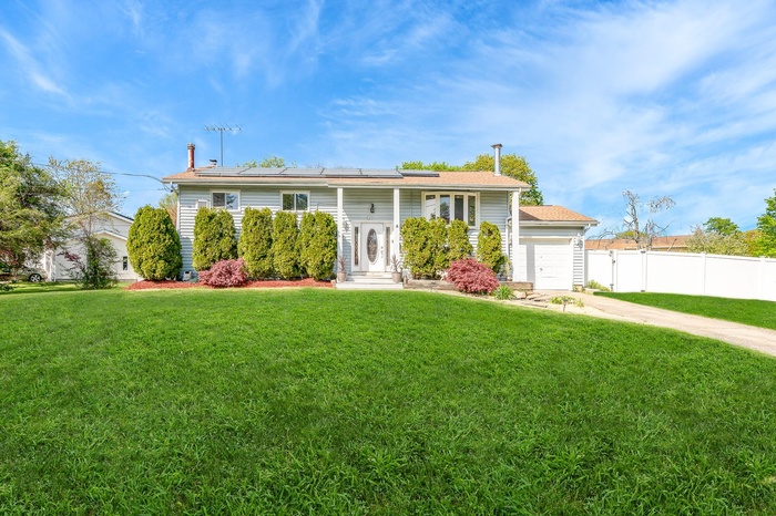 Raised ranch with an attached garage, a front lawn, fence, and solar panels