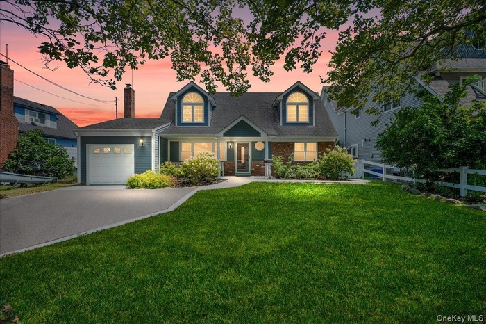 Cape cod house with a garage, driveway, brick siding, and a chimney