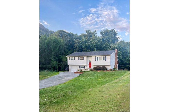 Bi-level home with driveway, an attached garage, a front lawn, a chimney, and a wooded view
