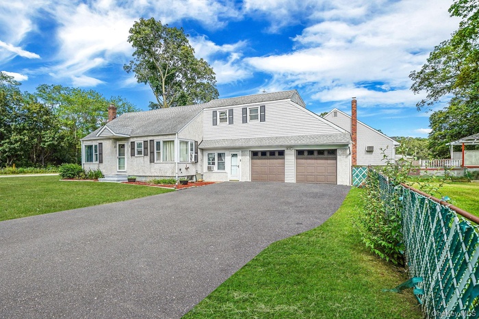 View of front facade featuring a chimney, asphalt driveway, a shingled roof, and a garage