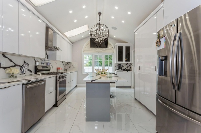 Kitchen with appliances with stainless steel finishes, modern cabinets, wall chimney range hood, white cabinets, and a chandelier