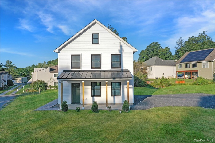 View of front of house featuring a standing seam roof, a metal roof, driveway, covered porch, and a front lawn