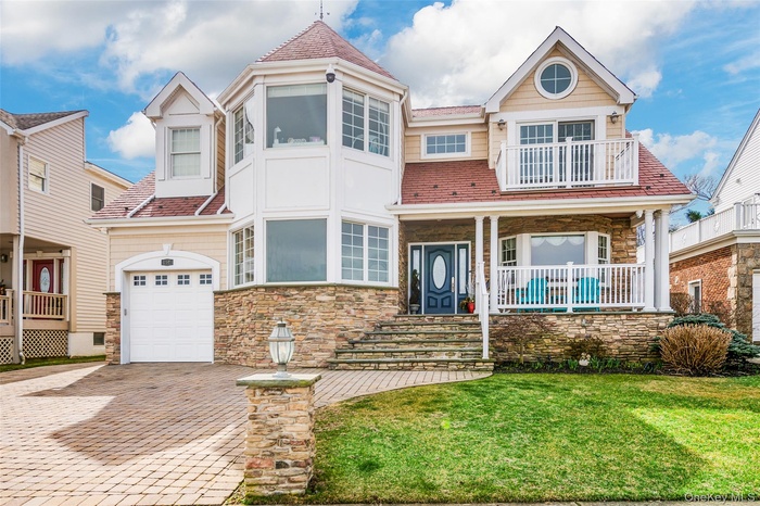 View of front of property with covered porch, stone siding, a front yard, and decorative driveway