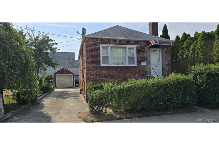 View of front of house featuring an outbuilding, concrete driveway, brick siding, and a chimney
