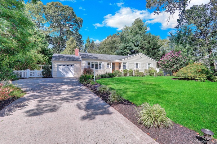 Ranch-style house with a garage, a chimney, concrete driveway, view of scattered trees, and a gate