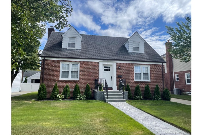 Brick Cape cod home with a front lawn and manicured landscaping.