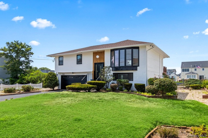Raised ranch with driveway, brick siding, a garage, and a front yard