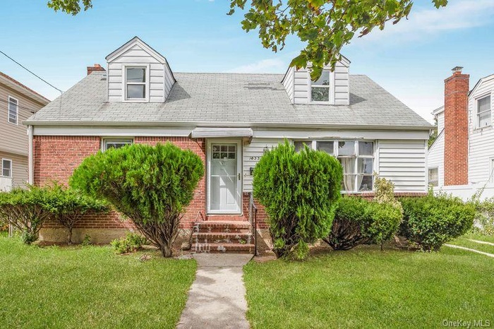 Cape cod home with a front yard, brick siding, and a shingled roof