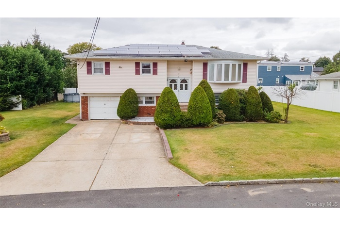Bi-level home featuring brick siding, an attached garage, roof mounted solar panels, and driveway