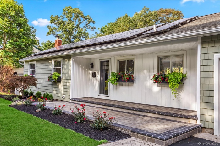 Doorway to property with solar panels, a chimney, roof with shingles, a yard, and covered porch