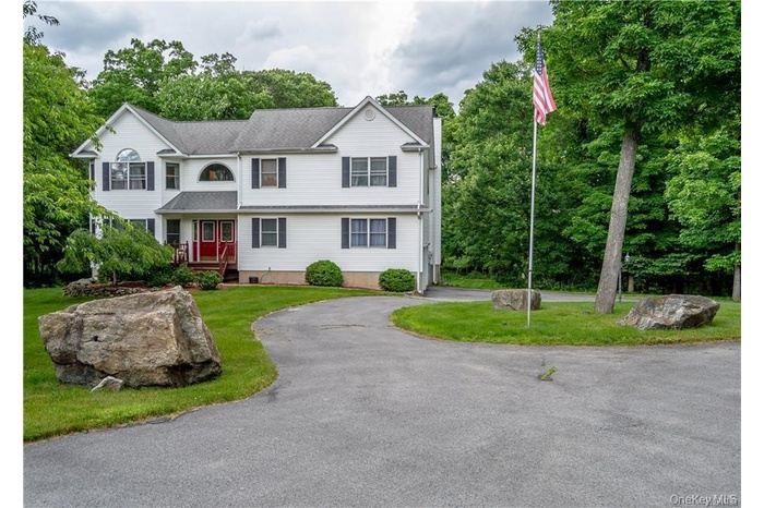 View of front of property featuring curved driveway, a front yard, and view of wooded area