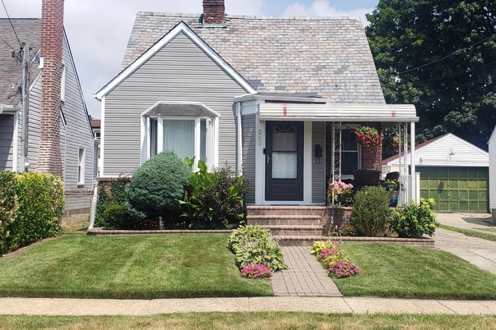 View of front facade with an outbuilding, a chimney, a front lawn, and a garage
