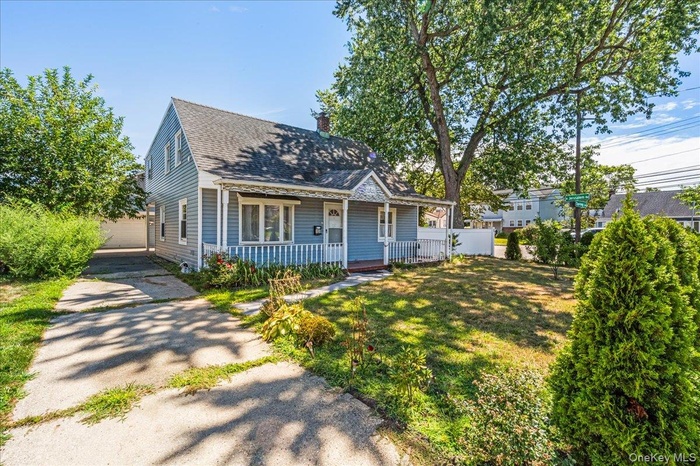 View of front of home with a porch, a chimney, a shingled roof, an outbuilding, and a front lawn