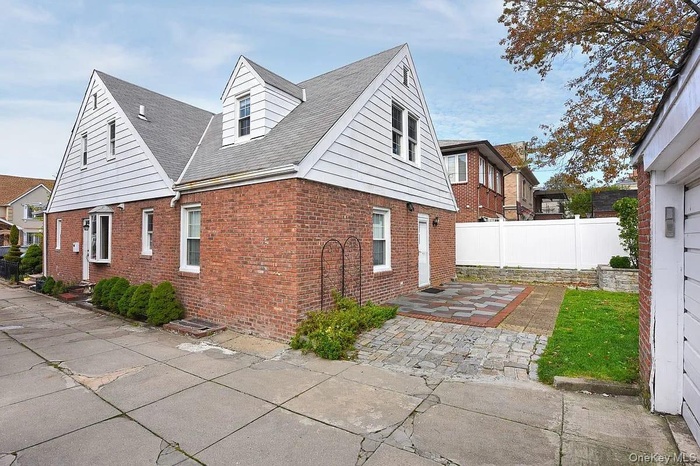 View of side of property with a patio, brick siding, and roof with shingles