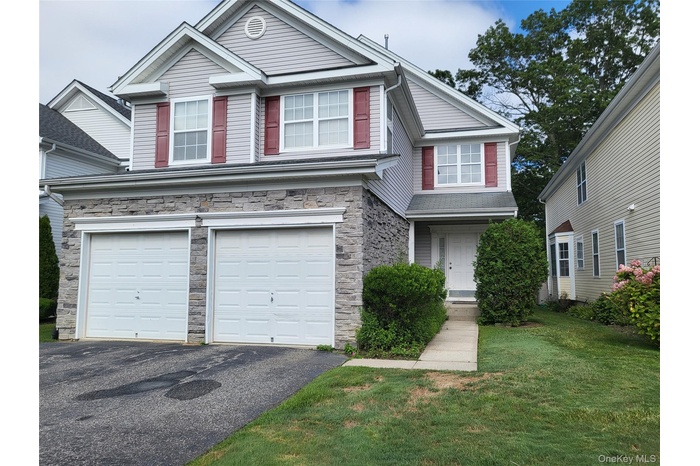 View of front of home featuring an attached garage, asphalt driveway, a front lawn, and stone siding