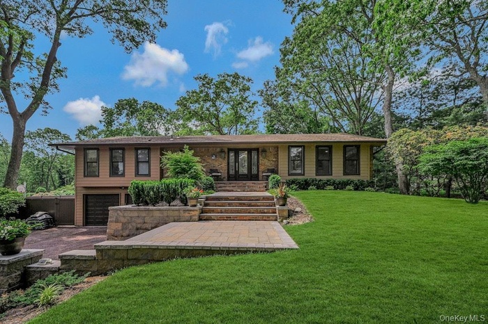 View of front of property with driveway, an attached 2 car garage, and lush landscaping.