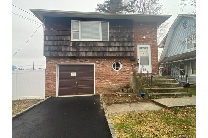 Tri-level home featuring an attached garage, brick siding, driveway, and mansard roof