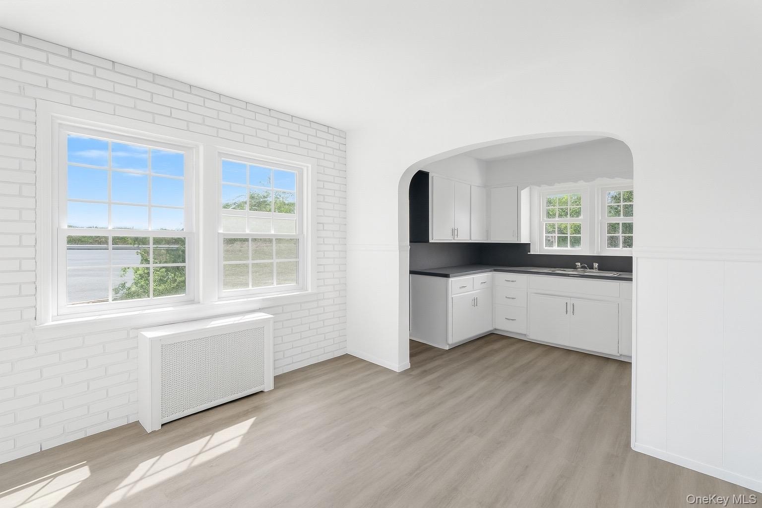Kitchen featuring dark countertops, light wood-style flooring, radiator, white cabinetry, and brick wall