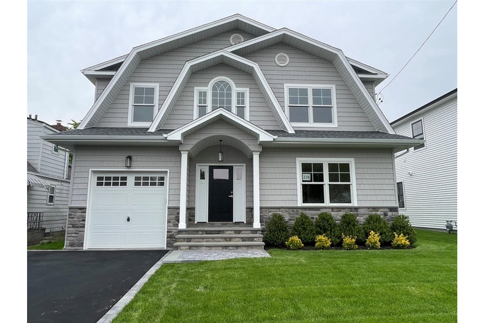 Dutch colonial featuring a gambrel roof, stone siding, and a front yard