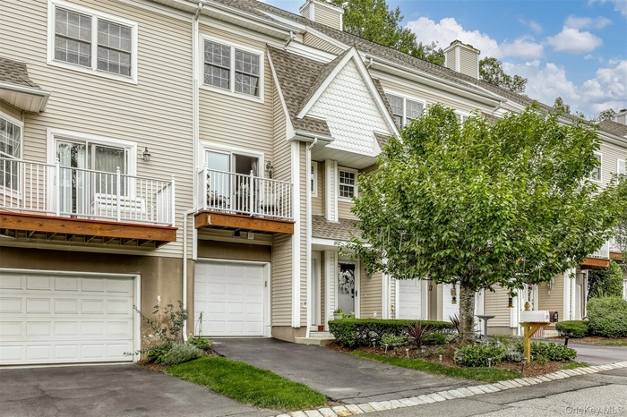 View of front of house with a balcony, a garage, a chimney, a shingled roof, and driveway