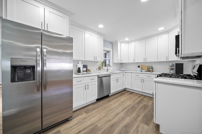 Kitchen featuring appliances with stainless steel finishes, white cabinets, light wood finished floors, recessed lighting, and light stone counters