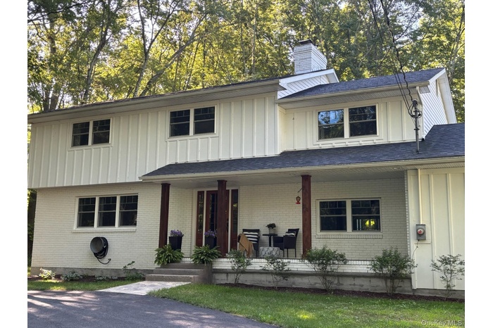 View of front of house with board and batten siding, a porch, a chimney, and brick siding