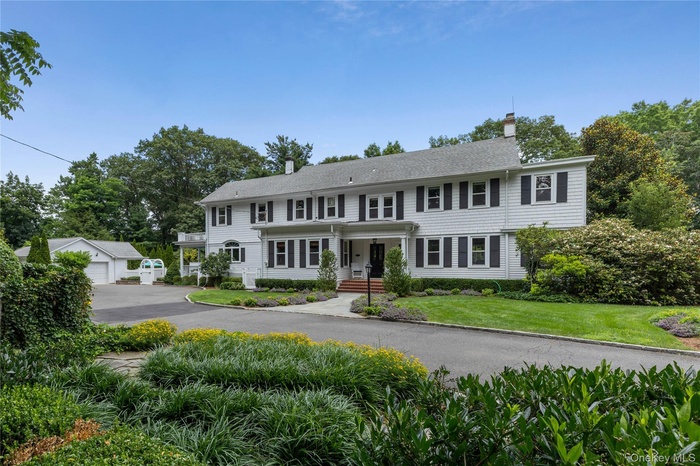 Colonial house featuring a chimney, a front lawn, an outbuilding, and a detached garage