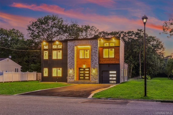 Modern home with driveway, a lawn, stone siding, and an attached garage