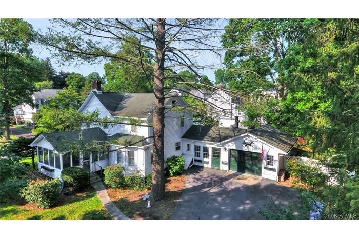 View of front of property featuring a sunroom, a chimney, driveway, an attached garage, and a shingled roof