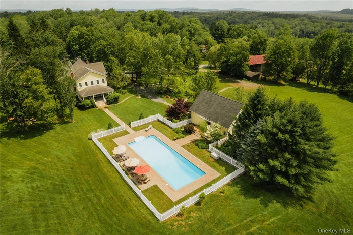 Aerial view of property and surrounding area with a pool area and a heavily wooded area
