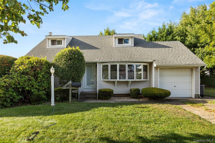 View of front facade with an attached garage, roof with shingles, a front yard, and a chimney