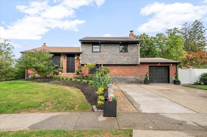 Split level home with a chimney, concrete driveway, an attached garage, and stone siding