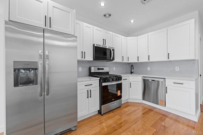 Kitchen with appliances with stainless steel finishes, tasteful backsplash, white cabinets, light wood-type flooring, and recessed lighting