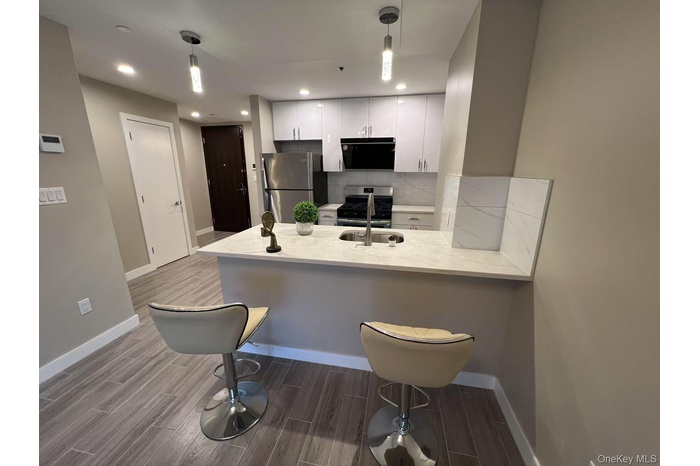 Kitchen featuring wood finish floors, appliances with stainless steel finishes, white cabinetry, a peninsula, and tasteful backsplash
