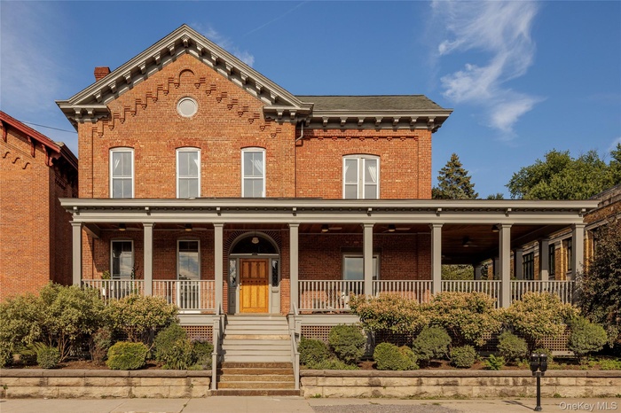 Italianate home featuring brick siding, covered porch, and stairs