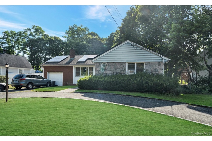 View of front of property with solar panels, gravel driveway, a chimney, a front lawn, and a garage