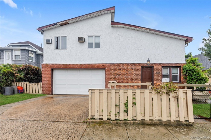 Traditional-style house featuring a fenced front yard, a garage, brick siding, concrete driveway, and stucco siding