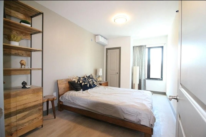 Bedroom with wood finished floors, an AC wall unit, and baseboards