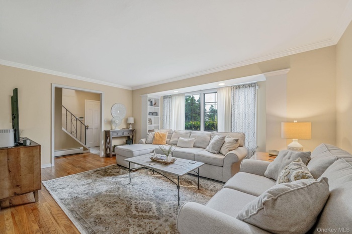 Living area with light wood-style flooring, crown molding, stairway, and a baseboard radiator