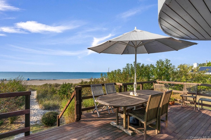 Wooden deck featuring outdoor dining space and view of water and beach