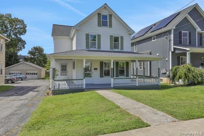 View of front facade featuring a porch, a front lawn, an outbuilding, and a garage